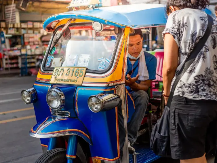 A driver in a blue and white tuk-tuk, picking up a passenger.